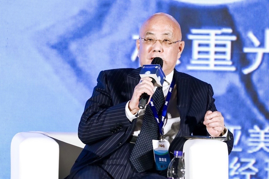 Бизнесмен Chongguan Lin сидит на стуле на конференции