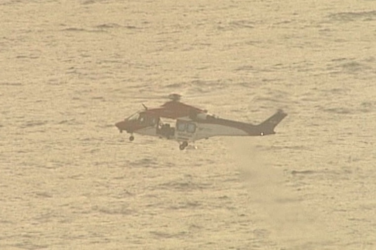 A helicopter flies above water in the early morning light, it's side door open.
