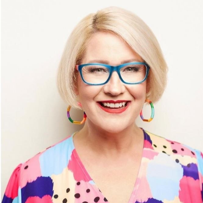  A smiling woman with short blonde hair, wearing colourful earings, glasses and top