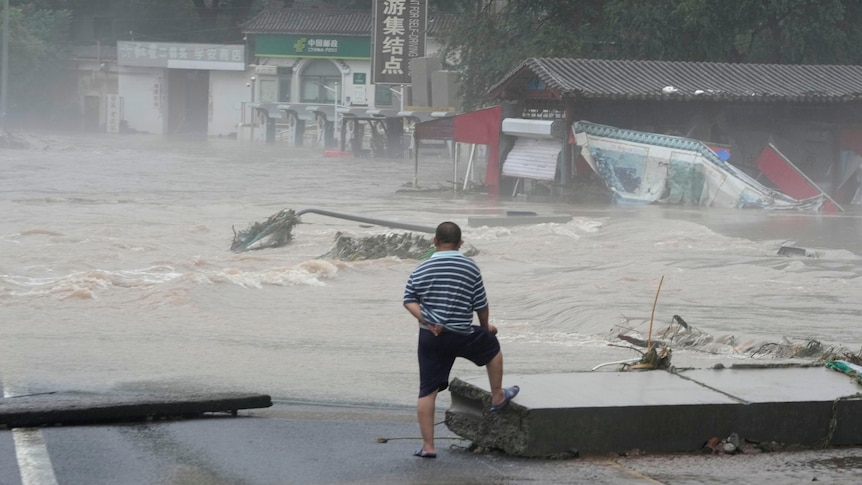 A man stares out at raging floodwaters in a village.