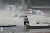 A man stares out at raging floodwaters in a village. 