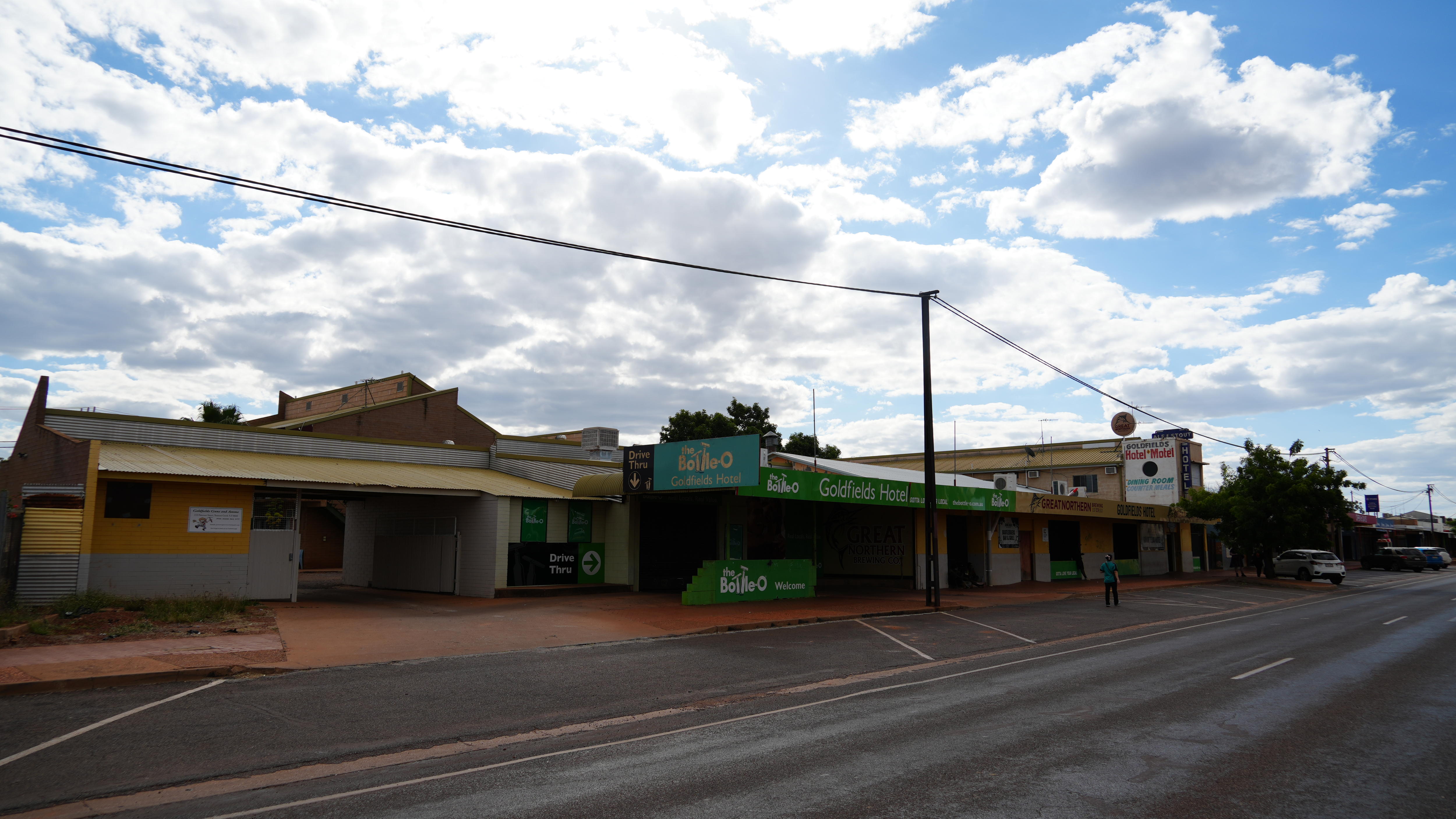 A wide shot of a street in a small town, with only a few cars seen edge of frame and one person walking.