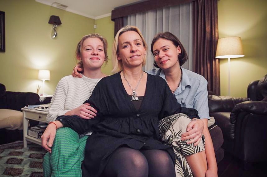 A woman with her hands on the knees of two teenaged girls