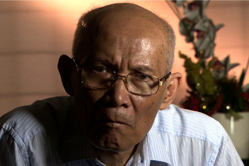 Close up of older Indonesian man wearing glasses and a blue-striped shirt.