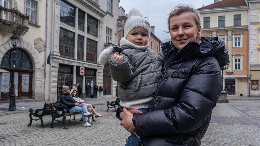 A woman holds a baby outdoors. Both wear parkers