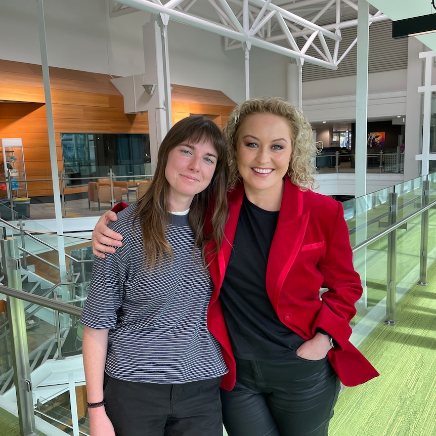 Angie Mcmahon wearing a grey top and black jeans next to Zan Rowe wearing a red jacket, black top and black jeans