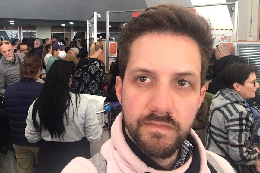 A man standing amid a large crowd inside an international airport