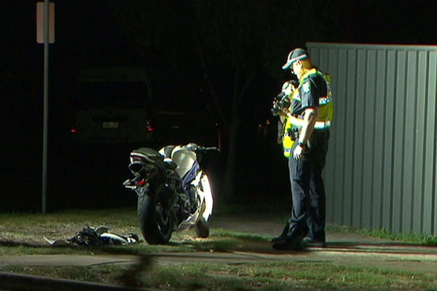 A police officer stands next to a motorcycle on a footpath at night