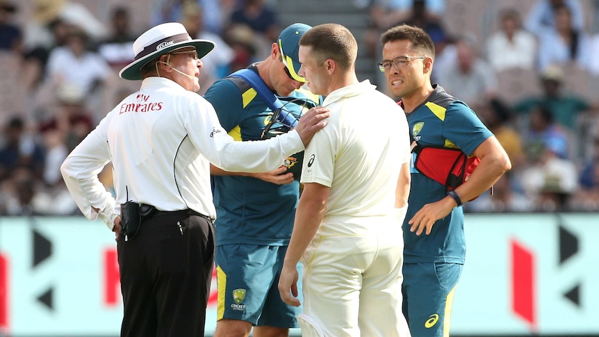 Marcus Harris is checked by the umpire and Australia team physios after a knock to the helmet