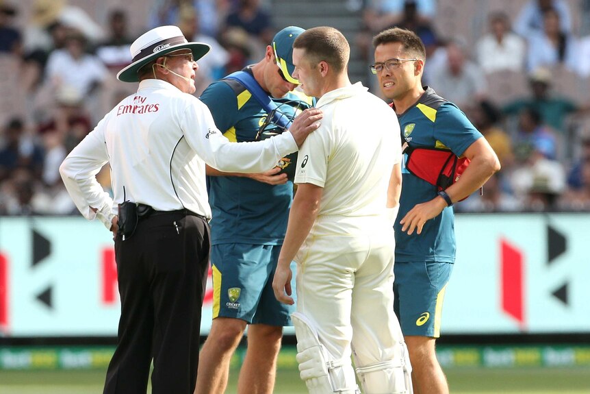 Marcus Harris is checked by the umpire and Australia team physios after a knock to the helmet