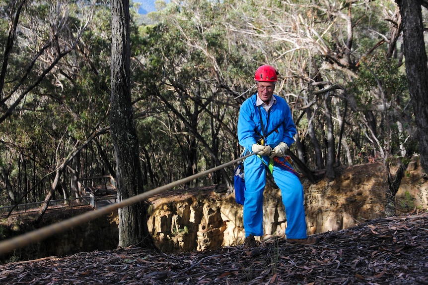 A man in bright blue overalls prepares to abseil back into the big hole