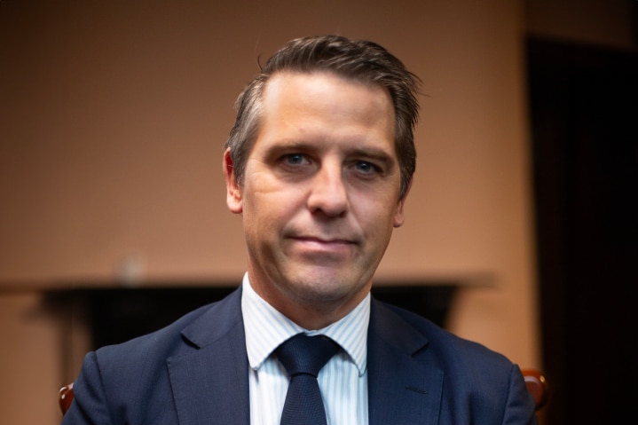 A man in a suit sits and smiles for the camera