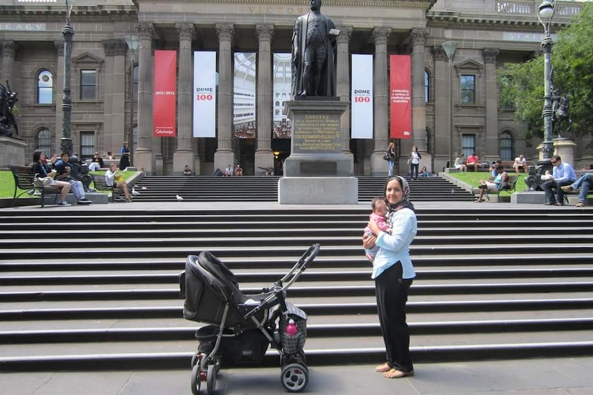 picture of a woman holding a child an her arms in front of the Victoria State Library building in Melbourne 