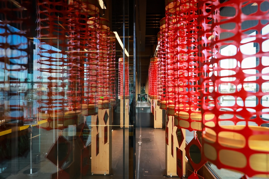 Columns of red safety mesh hang from a narrow glass-enclosed space.