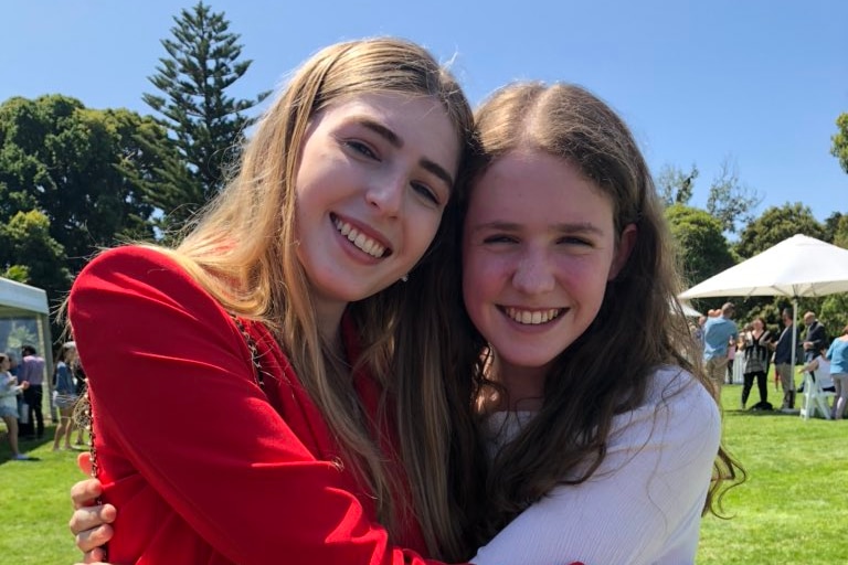 Two teenage girls hug tight outdoors at an event