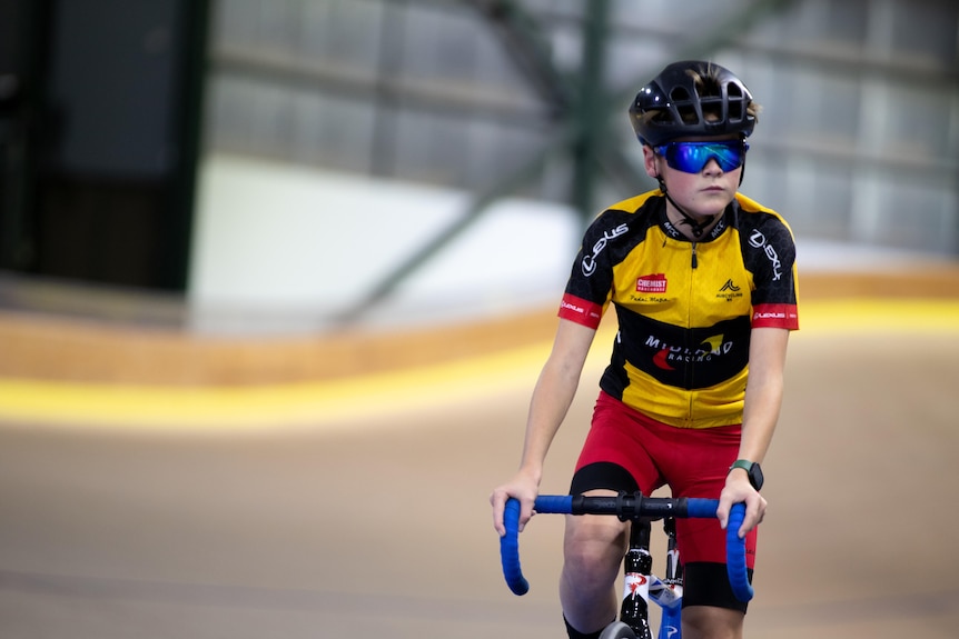 Boy in cycling gear looking focused while cycling in a velodrome.