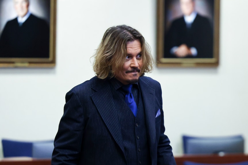 Johnny Depp with long hair and blue tie in courtroom.
