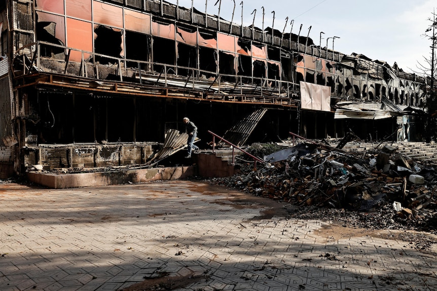 Man walks past charred building.