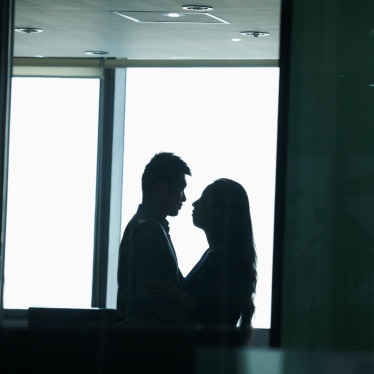 Two people standing close and looking into each other's eyes, in silhouette.