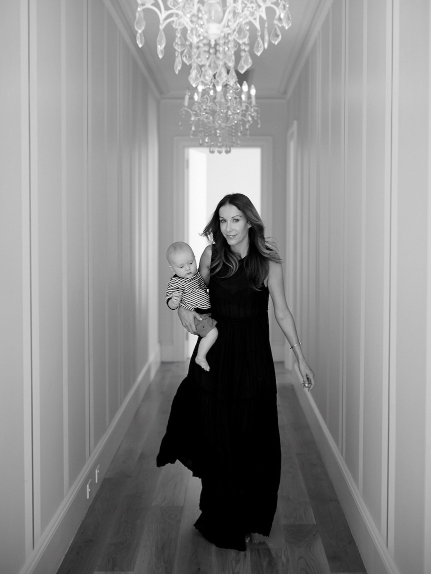 A woman walks down a hallway with a baby boy on her hip.