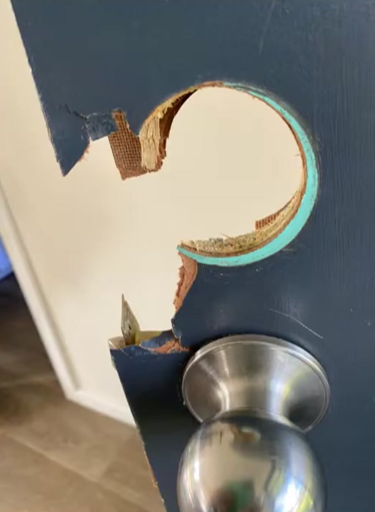 A section of a blue wooden door is missing where a lock once was installed above a silver handle.