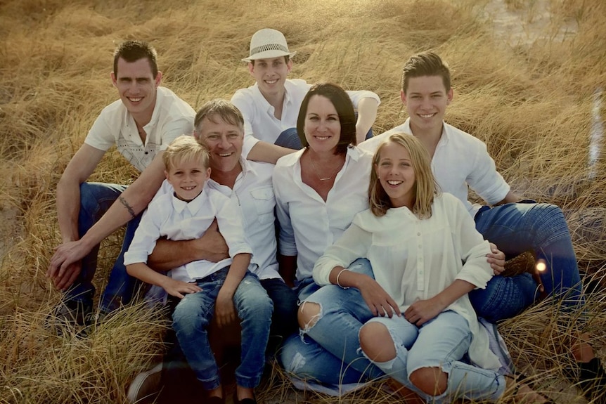 A family of seven sits in a field.