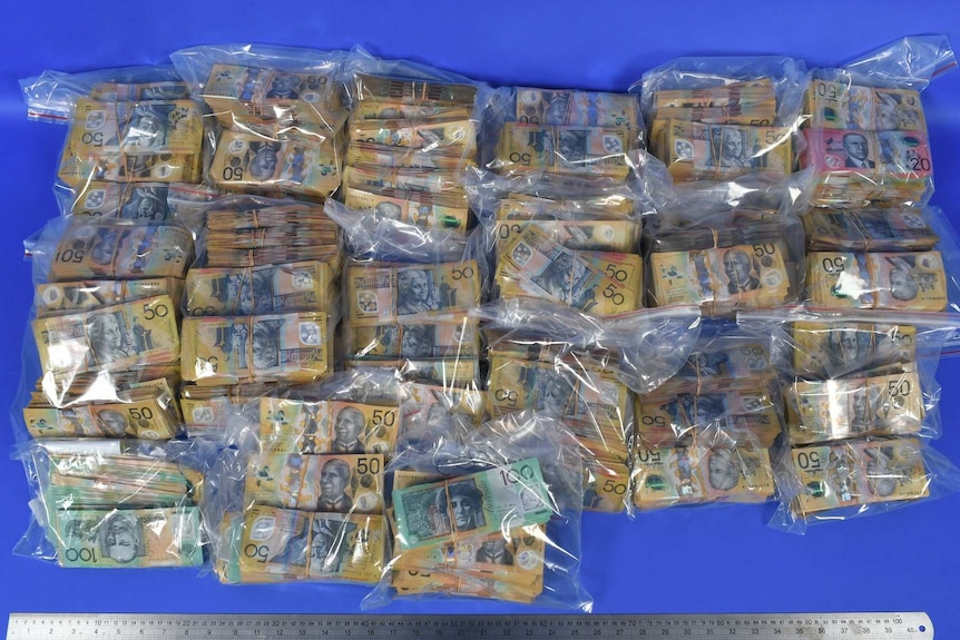 Big wads of $50 notes in plastic bags lying on a blue table.