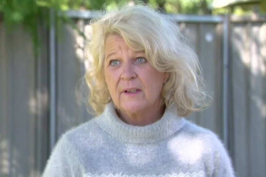 A woman with blonde hair and a grey jumper standing outside.