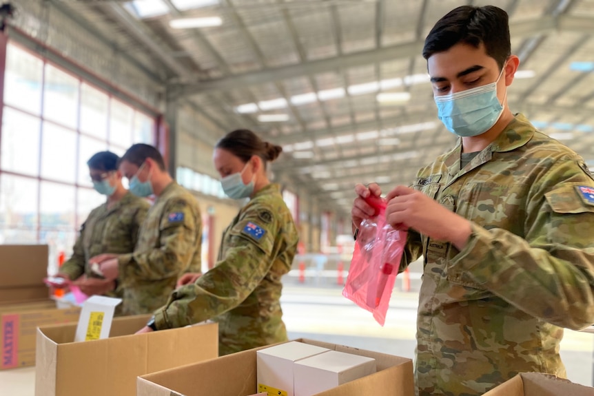 A line of people in army uniform sorting boxes on a table