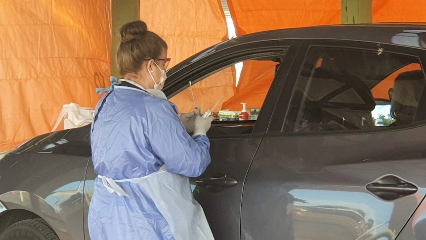 A coronavirus testing clinician stands at a car