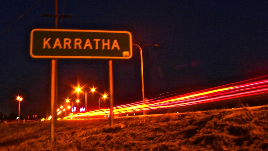 Sign for Karratha at night next to highway with traffic lights