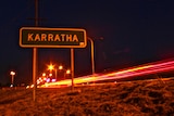 Sign for Karratha at night next to highway with traffic lights