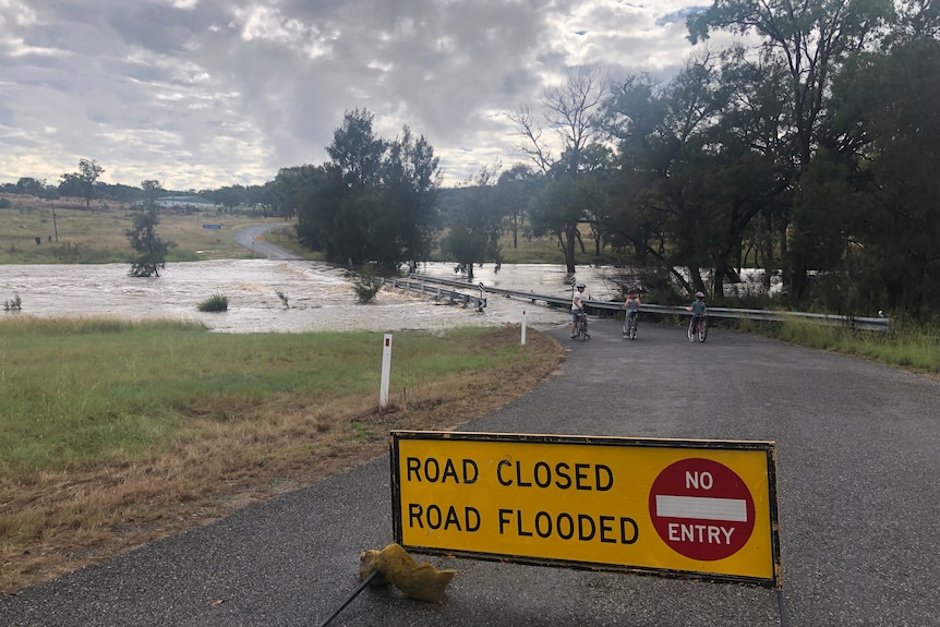 A road closed sign with a flooded bridge in the background. 