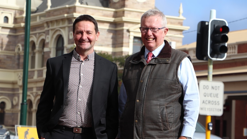Two men stand smiling in the streets of Broken Hill.