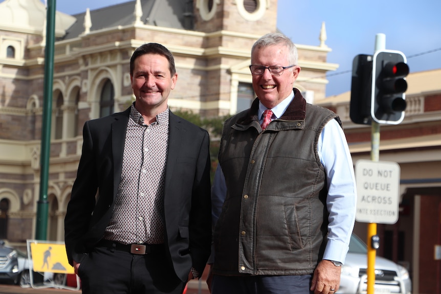 Two men stand smiling in the streets of Broken Hill.