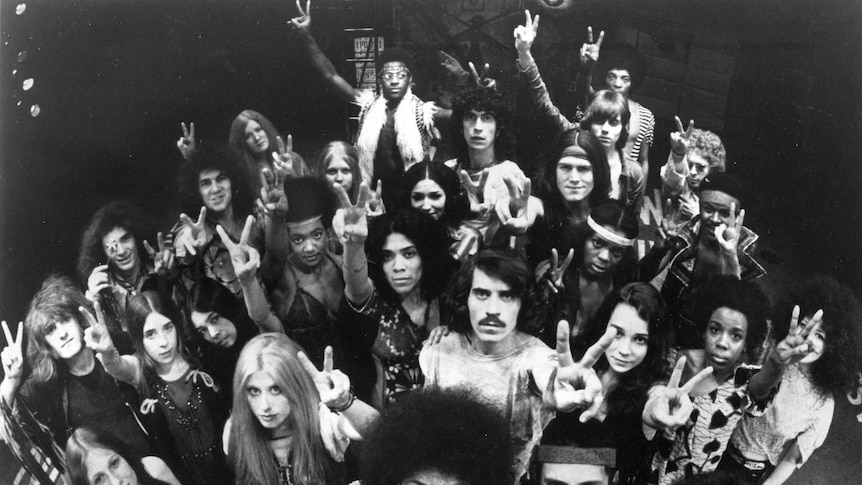 A black and white photo of the original broadway cast of hair all with their hands doing the peace sign