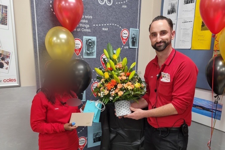 Daragh presents flowers to a female Coles team member, whose face has been blurred.