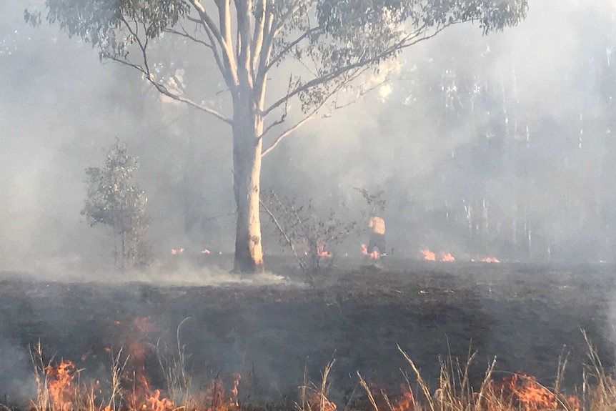 Looking through flames and heat haze at a fireman inspecting burnt ground