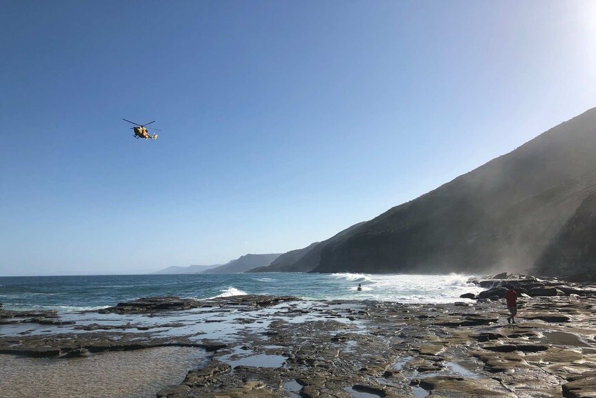 A yellow NSW surf life saving helicopter flies in blue skies over the figure eight rock pools at the Royal National Park.