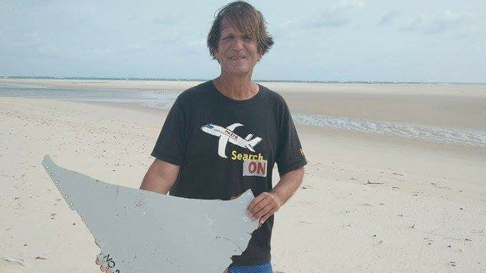 Blaine Gibson holds part of a wing on a beach.