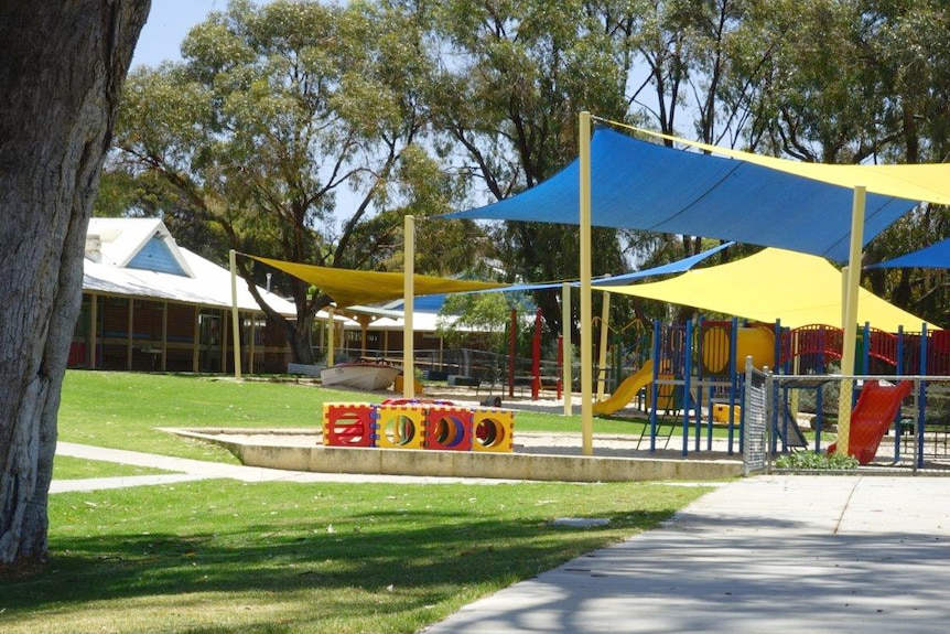 A wide shot of a school playground under blue and yellow shade sails with buildings in the background.