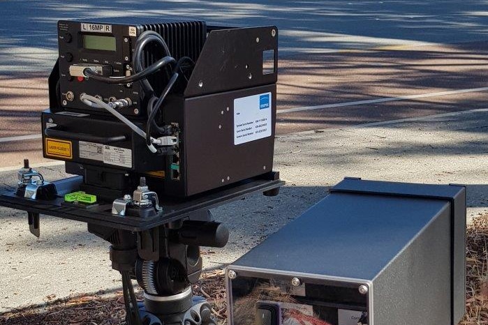 A speed camera set up on the side of a Perth road with a service station in the background.