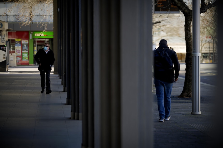 Two masked people walk down an otherwise dark and empty Canberra street.