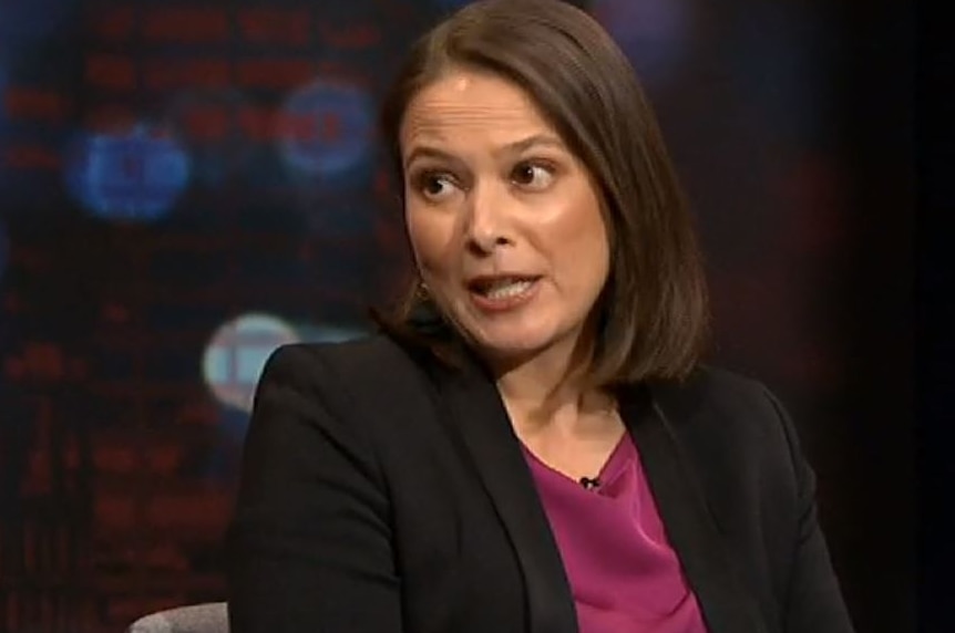 A woman with short hair in a dark suit and red top.