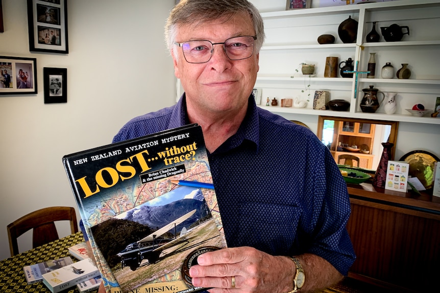 Richard in his living room holding his book Lost Without a Trace