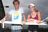 Two young tennis players pose for a photo standing by the net