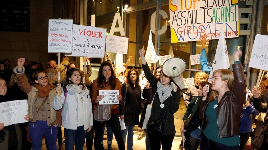 A group of female protestors hold signs outside a cinema.