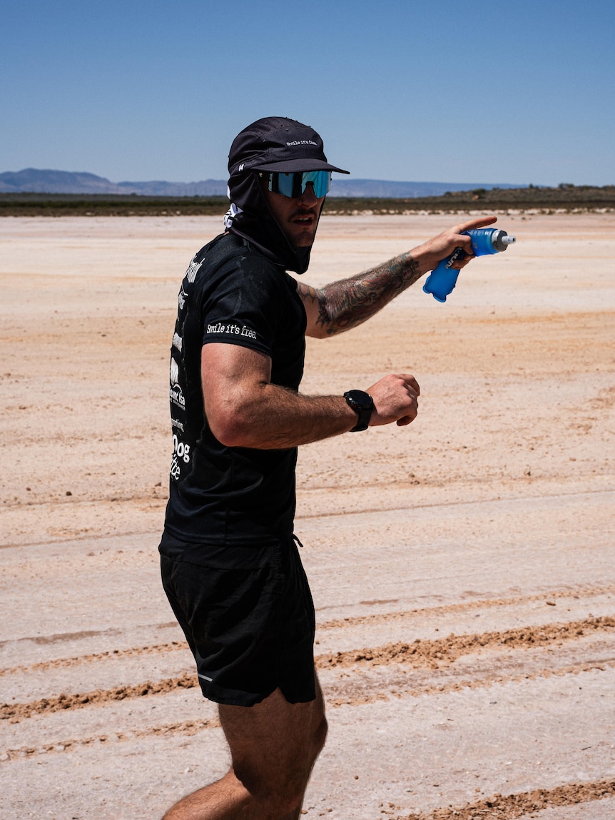 Man runs across desert with hat and glasses on. 