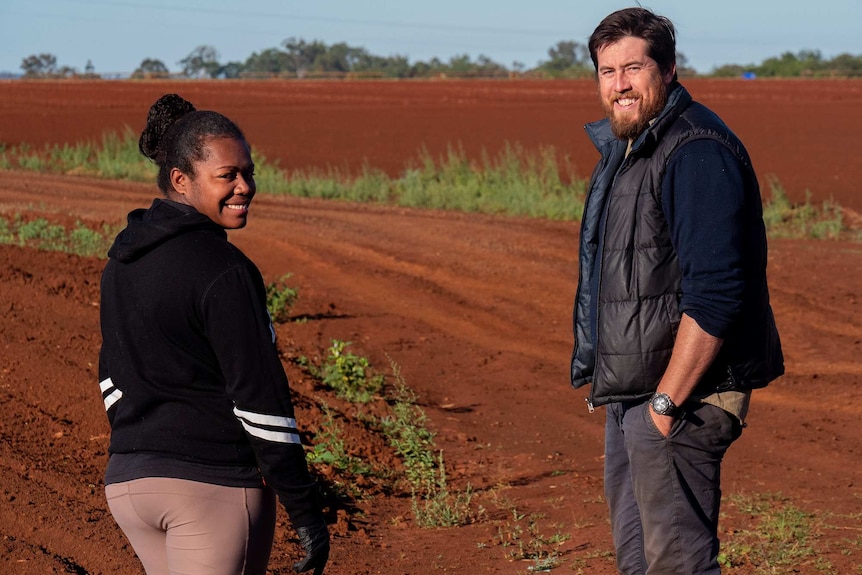A woman and man stand in a red dirt field.