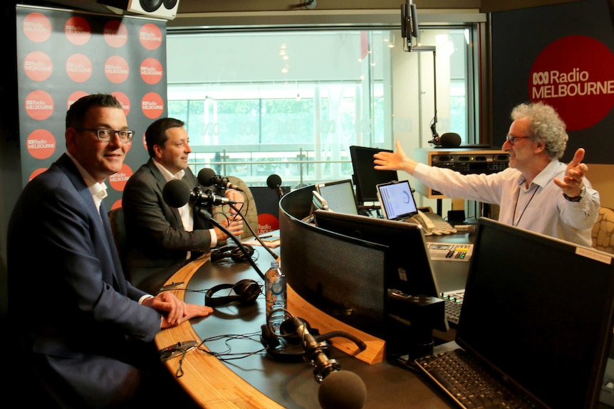 Daniel Andrews smiling as Matthew Guy looks at Jon Faine with his arms open wide.